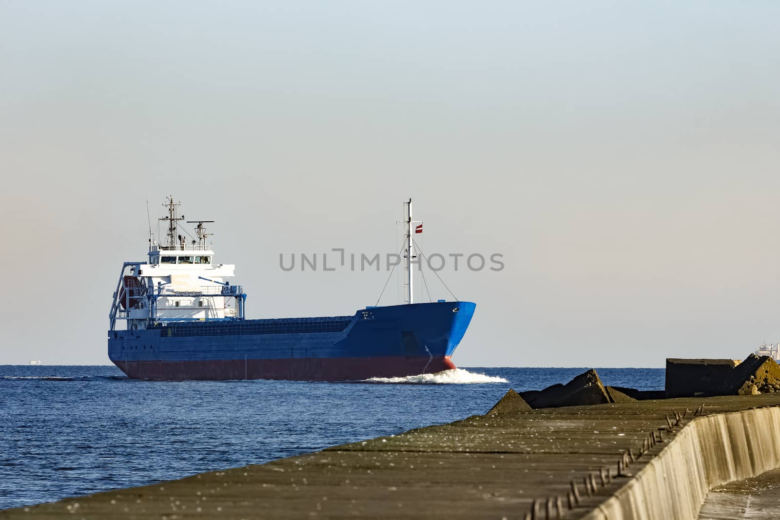 Blue cargo ship sailing against the breakwater dam