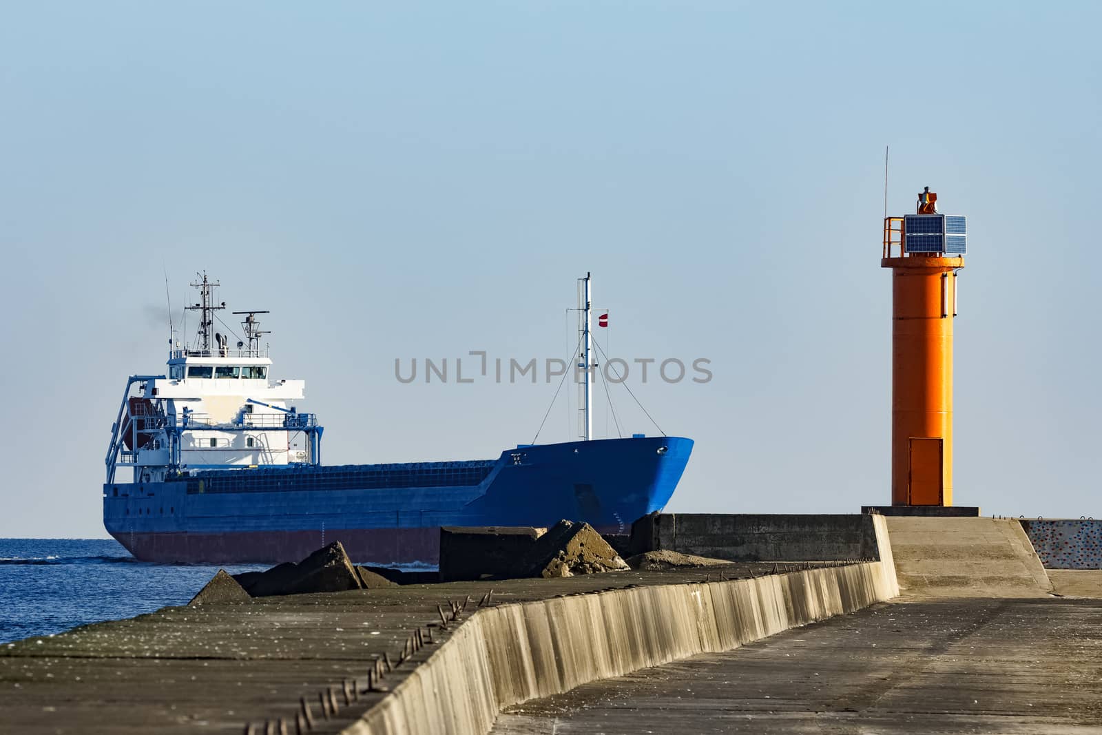 Blue cargo ship sailing against the breakwater dam