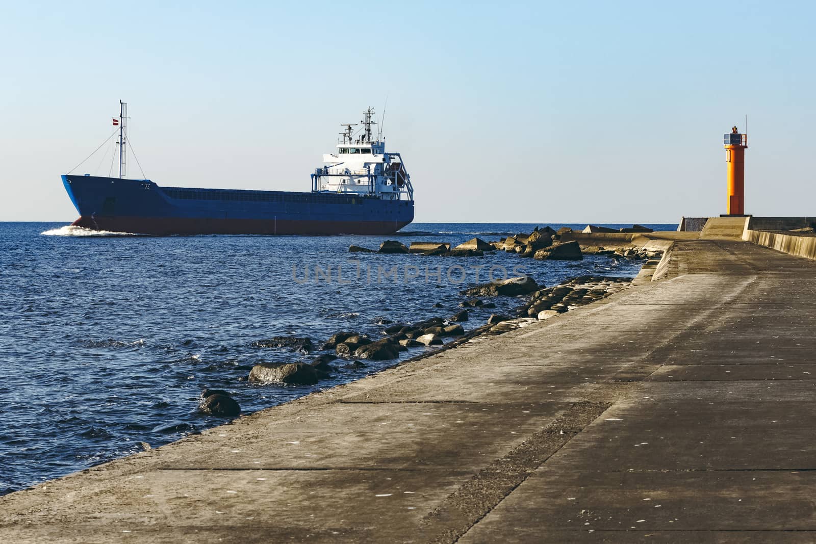 Blue cargo ship sailing against the breakwater dam