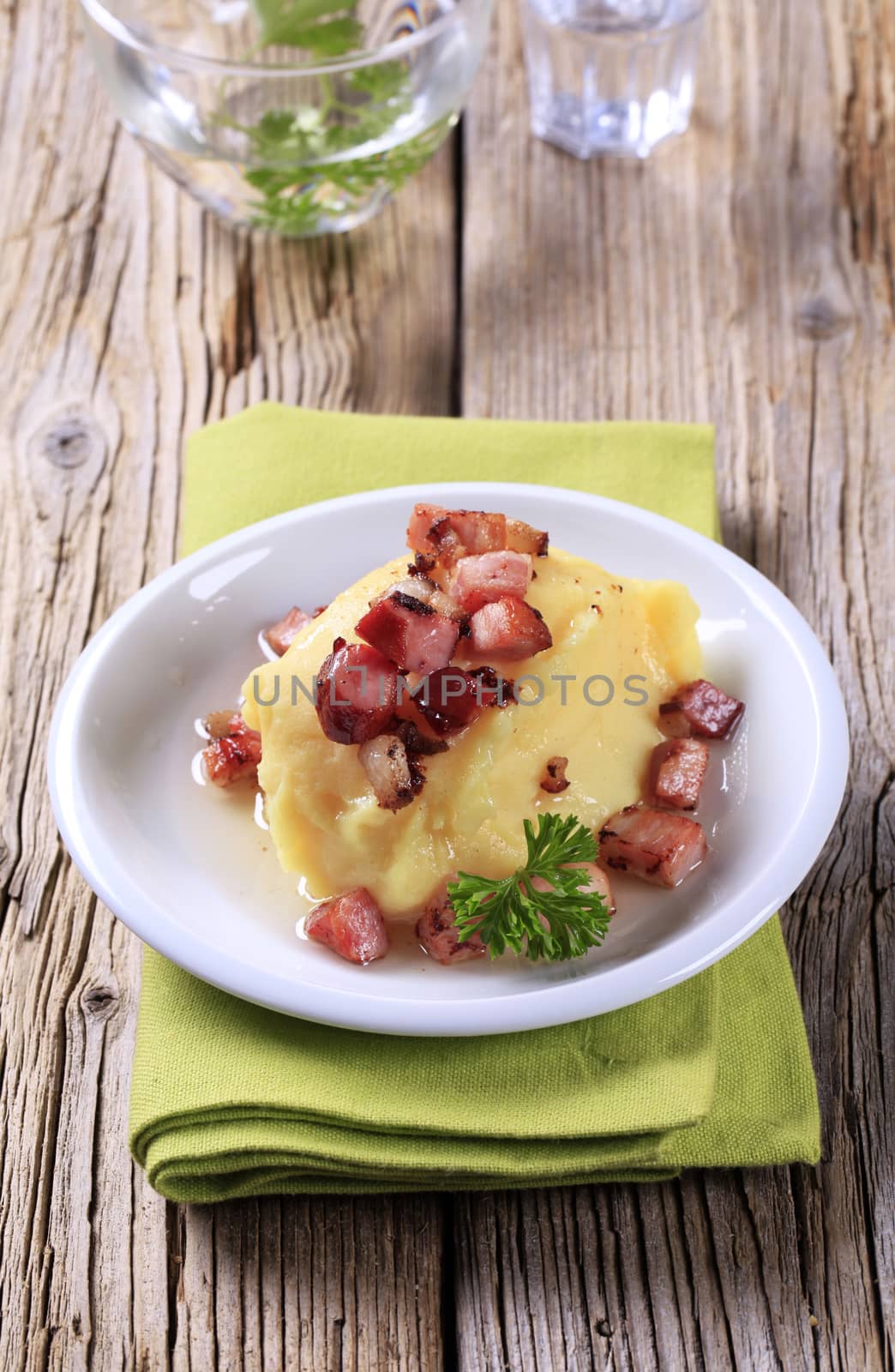 Dish of mashed potato and diced smoked pork on wooden background