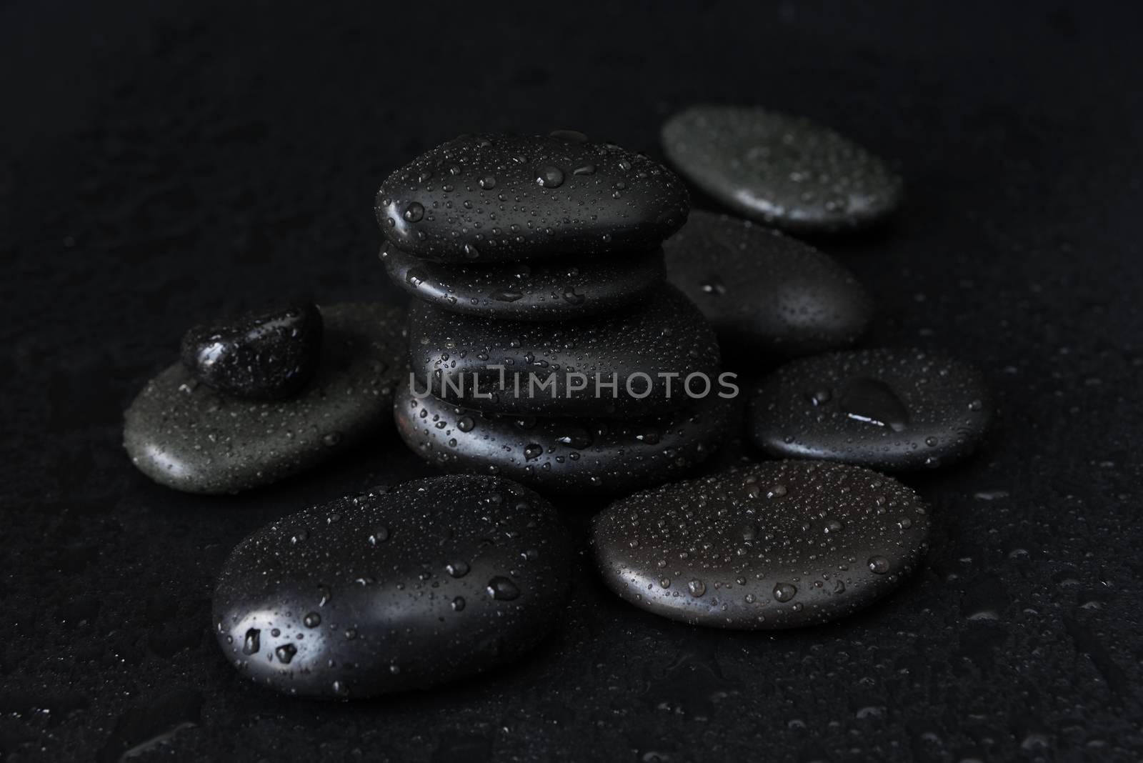 Spa concept with heap of the black basalt massage stones covered with water drops on a black background