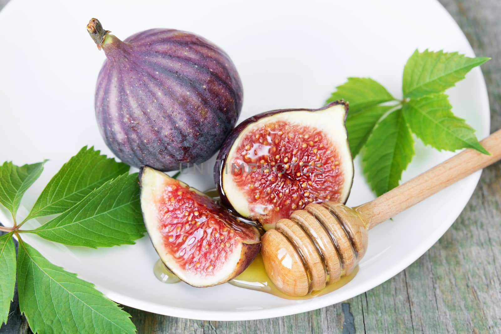 Ripe figs, fresh honey and beautiful green leaves are on a white porcelain plate