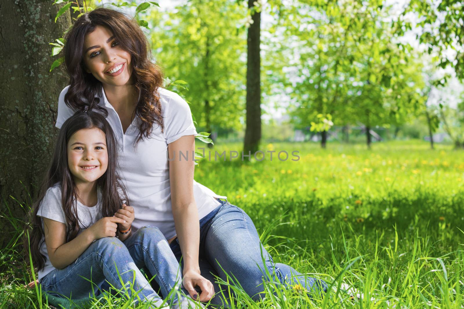 Beautiful young mother and daughter relaxing sitting on grass in park