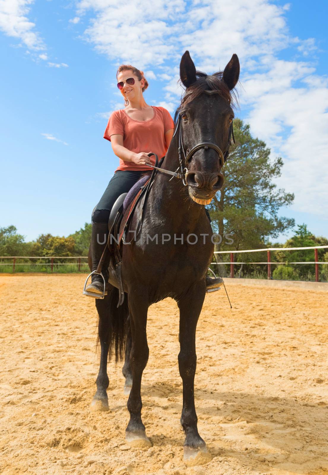 smiling riding girl and her black stallion in a training