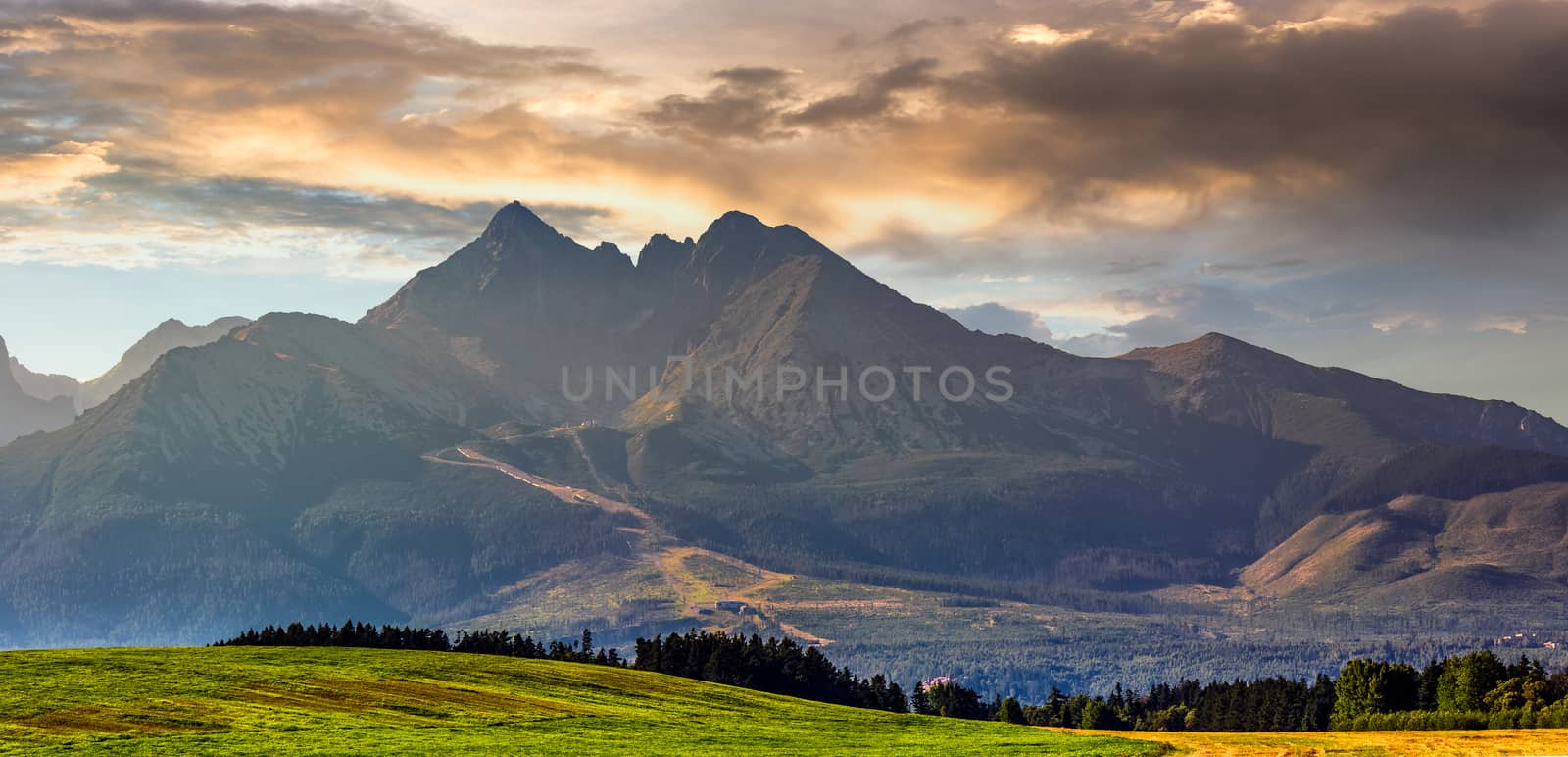 Panorama of Tatra mountains in evening haze behind the forest and rural field