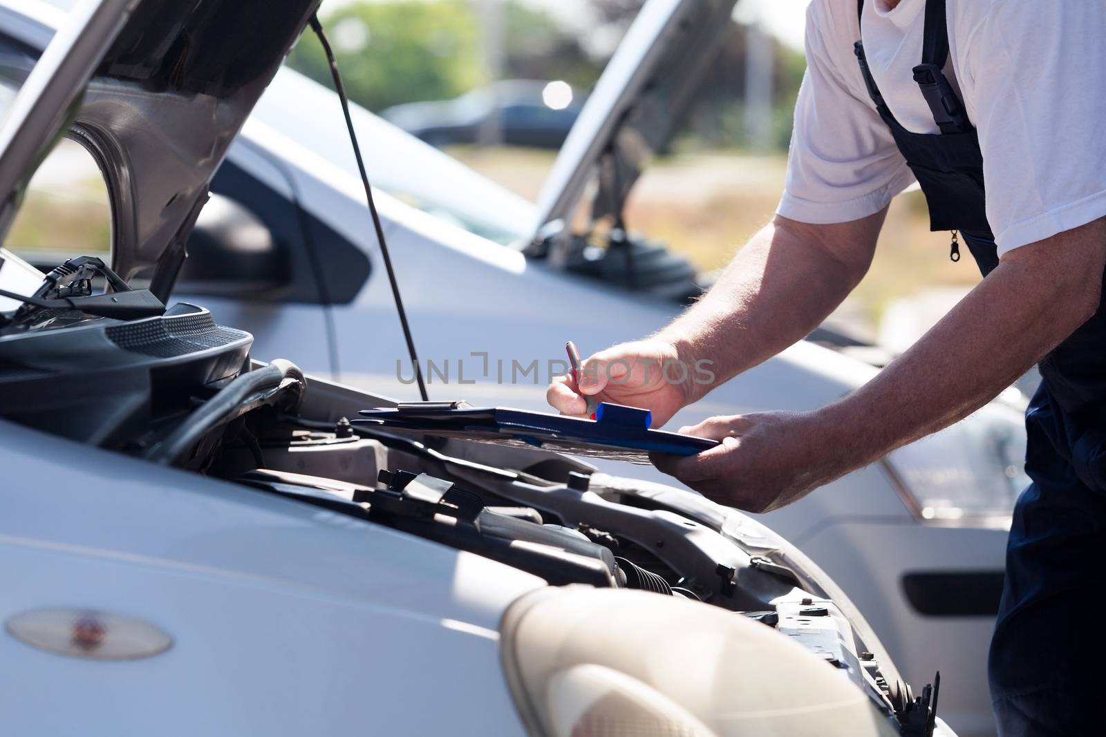 Auto mechanic checking car engine and writing on the clipboard by wellphoto