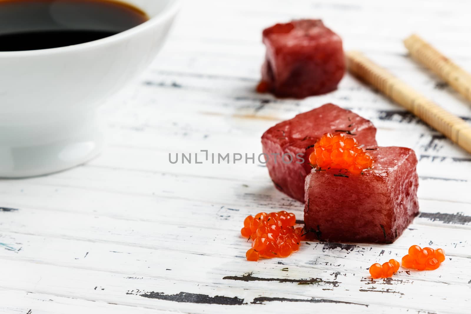 Tuna sashimi dipped in soy sauce with salmon roe on old white wooden board with chopsticks and bowl with soy. Raw fish in traditional Japanese style. Horizontal image.