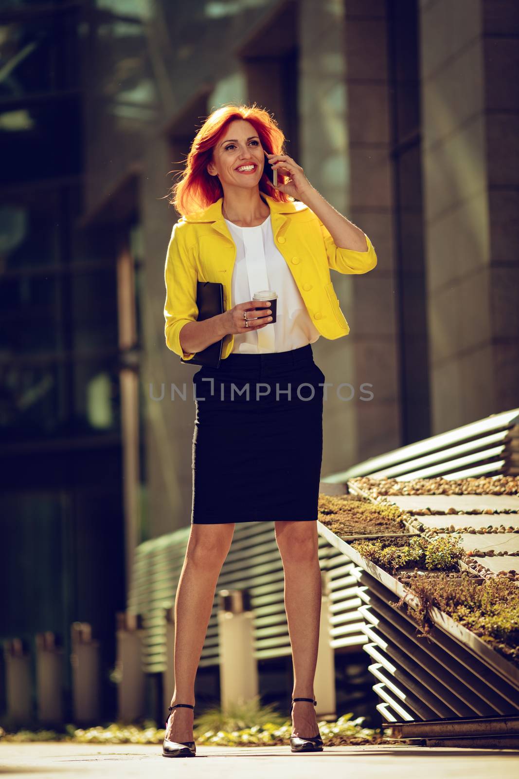 Smiling successful businesswoman using smartphone on coffee break in office district. Looking away.
