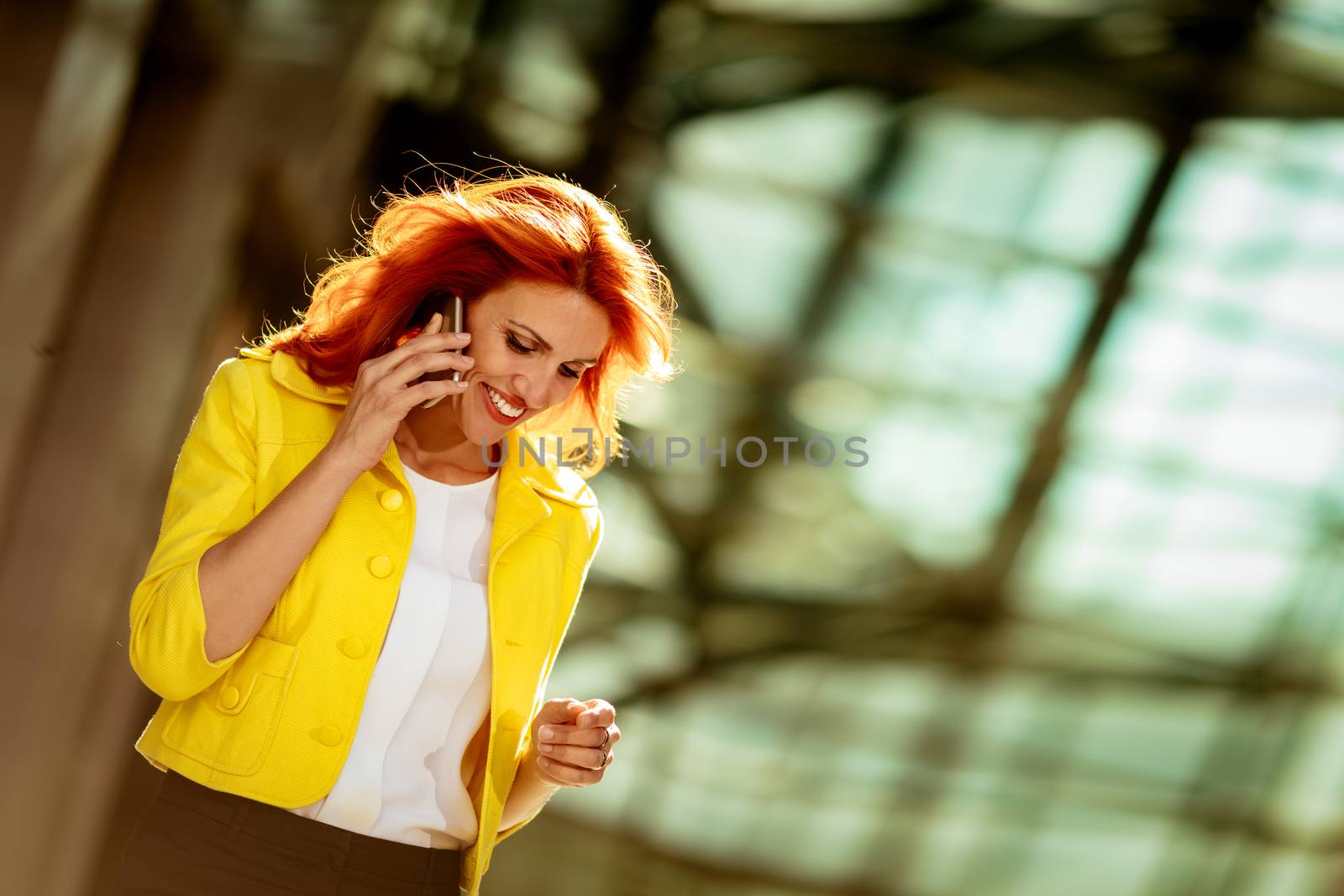Smiling successful businesswoman talking on smartphone in office district.