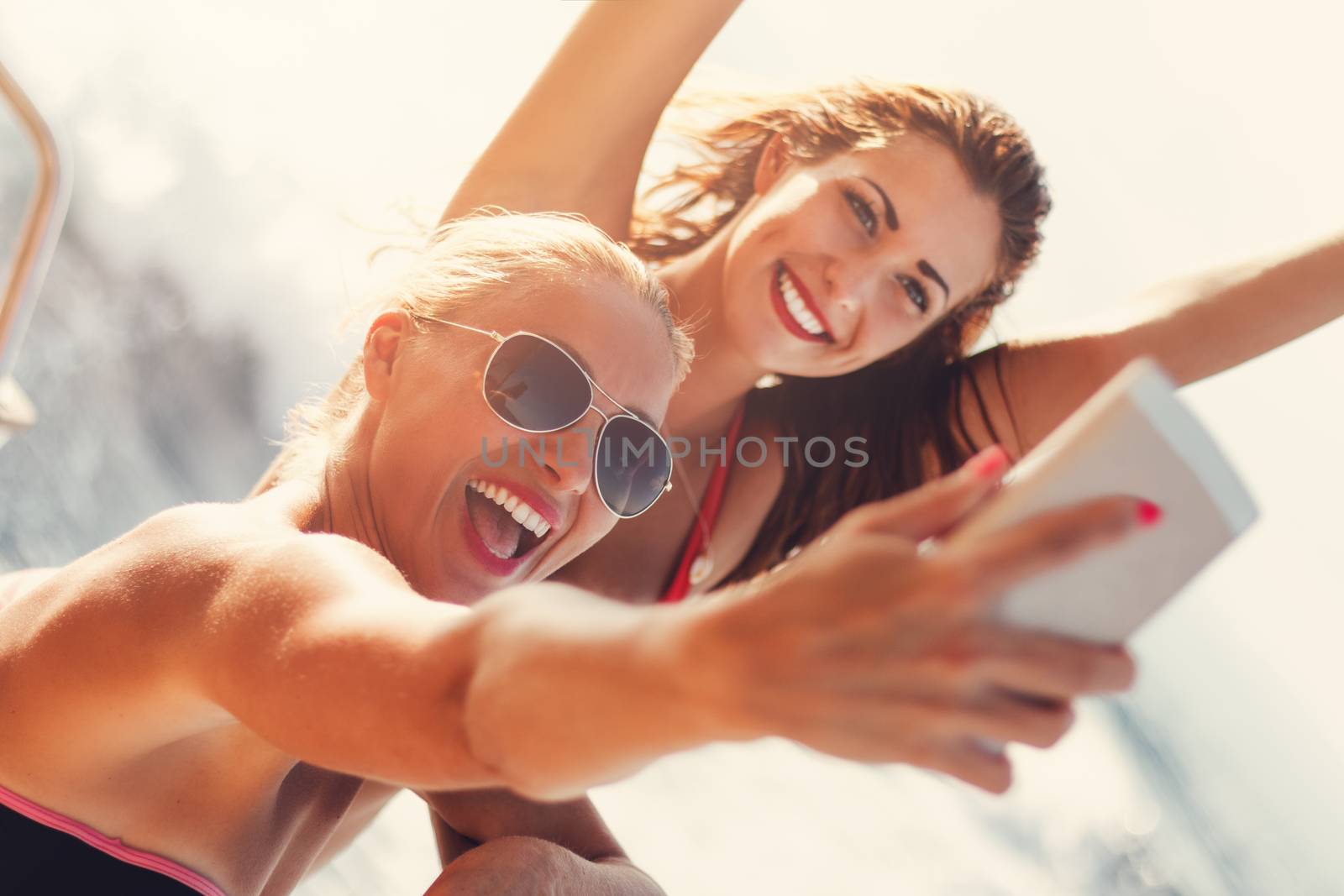 Young cheerful female friends taking a selfie while enjoying on a cruise.