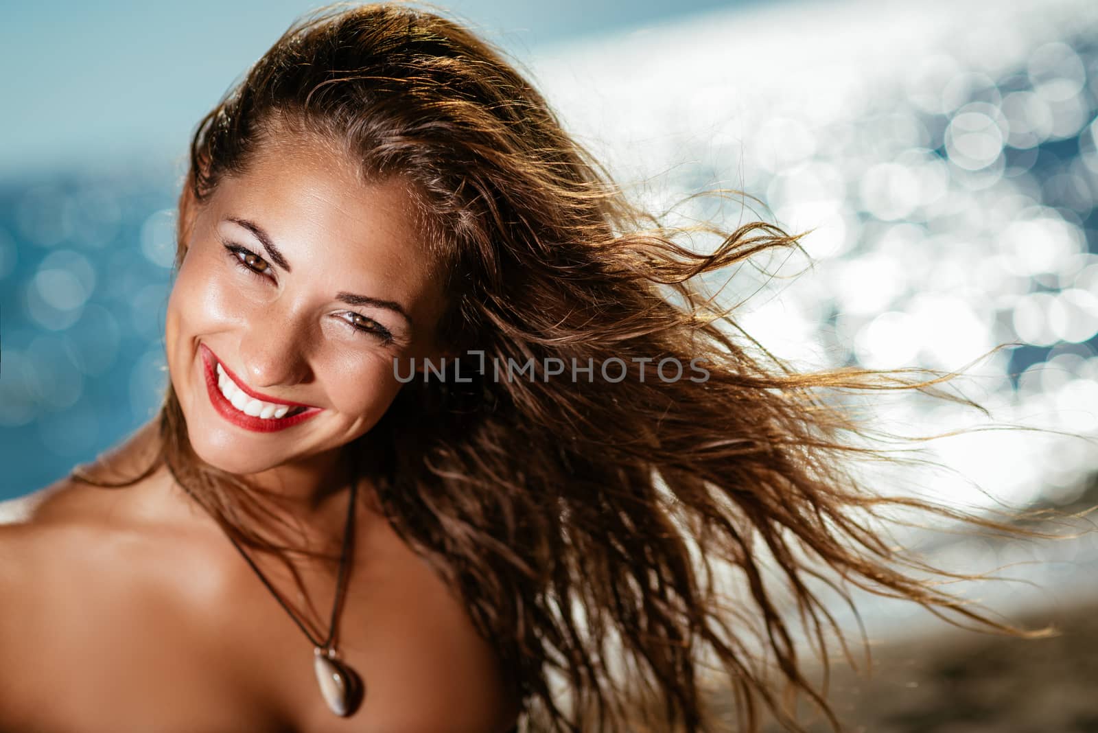 Portrait of a beautiful young woman enjoying on the beach. She is smiling and looking at camera.