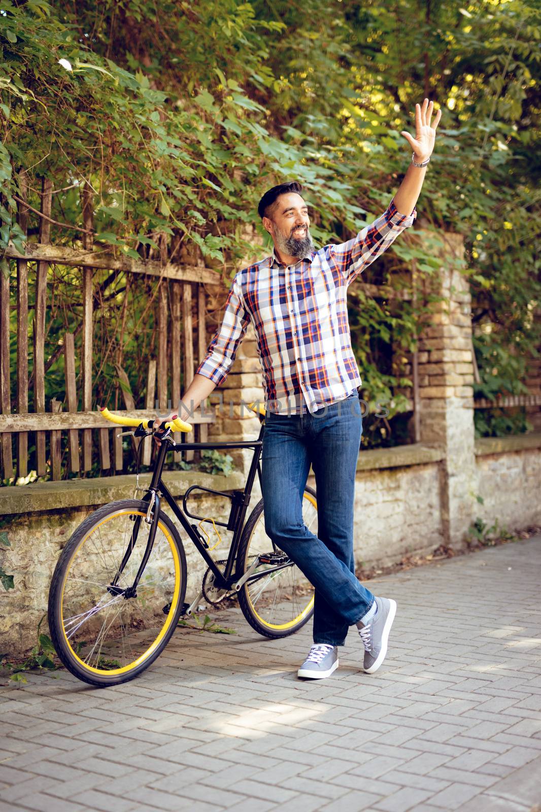 Casual businessman going to work by bicycle. He is walking next to bike and waving away.