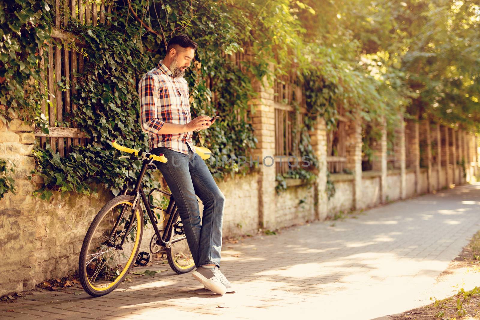 Casual businessman going to work by bicycle. He is standing next to bike and sending text message.