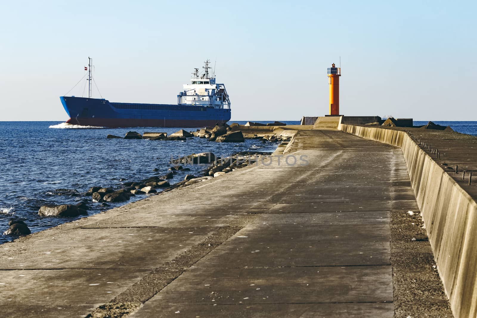 Blue cargo ship sailing against the breakwater dam