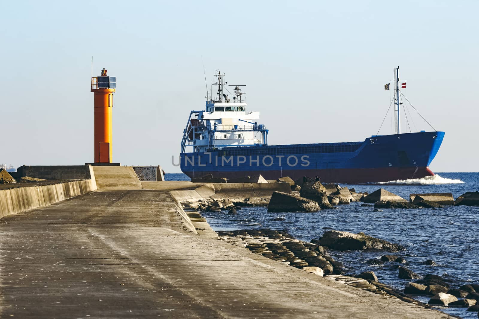 Blue cargo ship sailing against the breakwater dam
