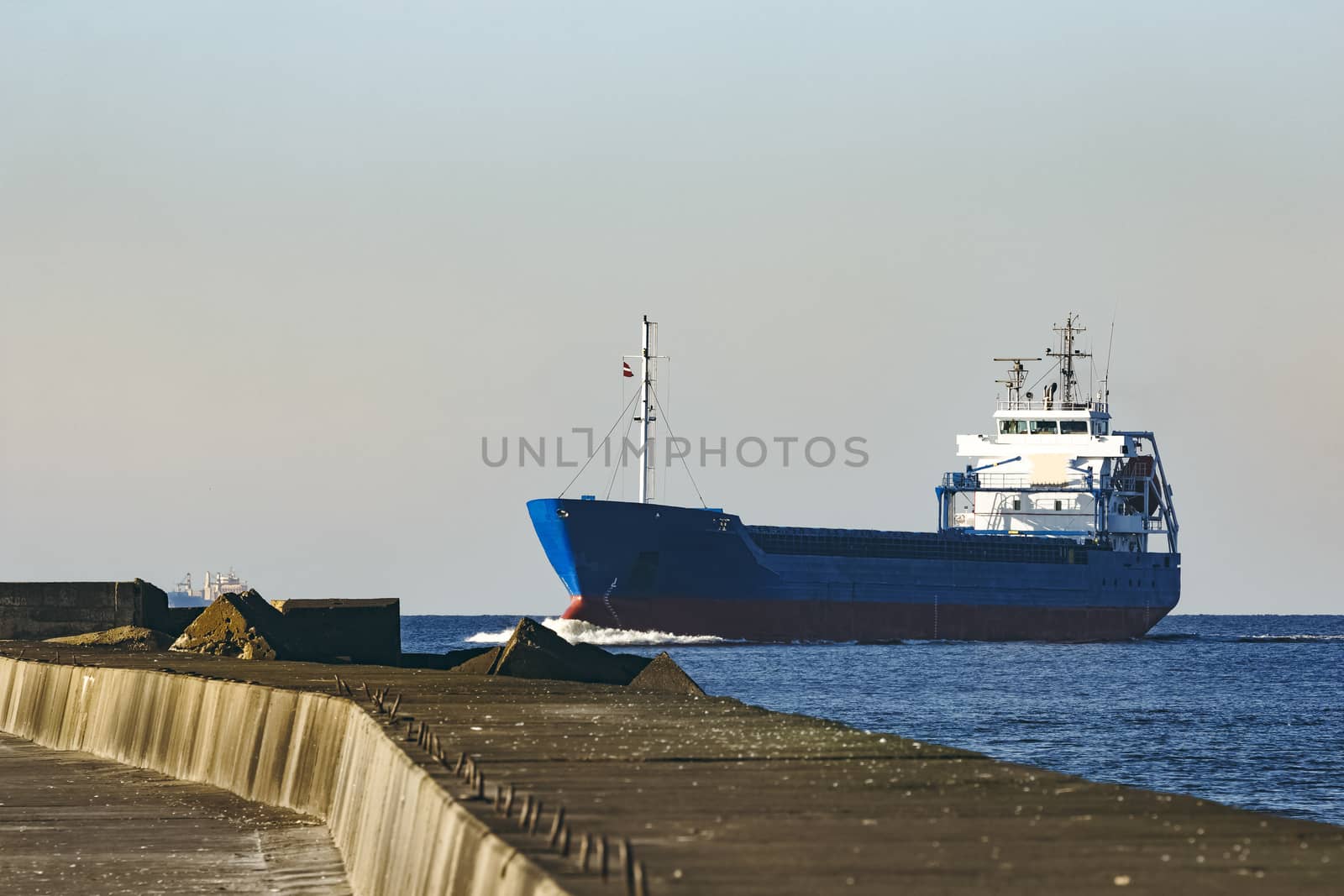 Blue cargo ship sailing against the breakwater dam