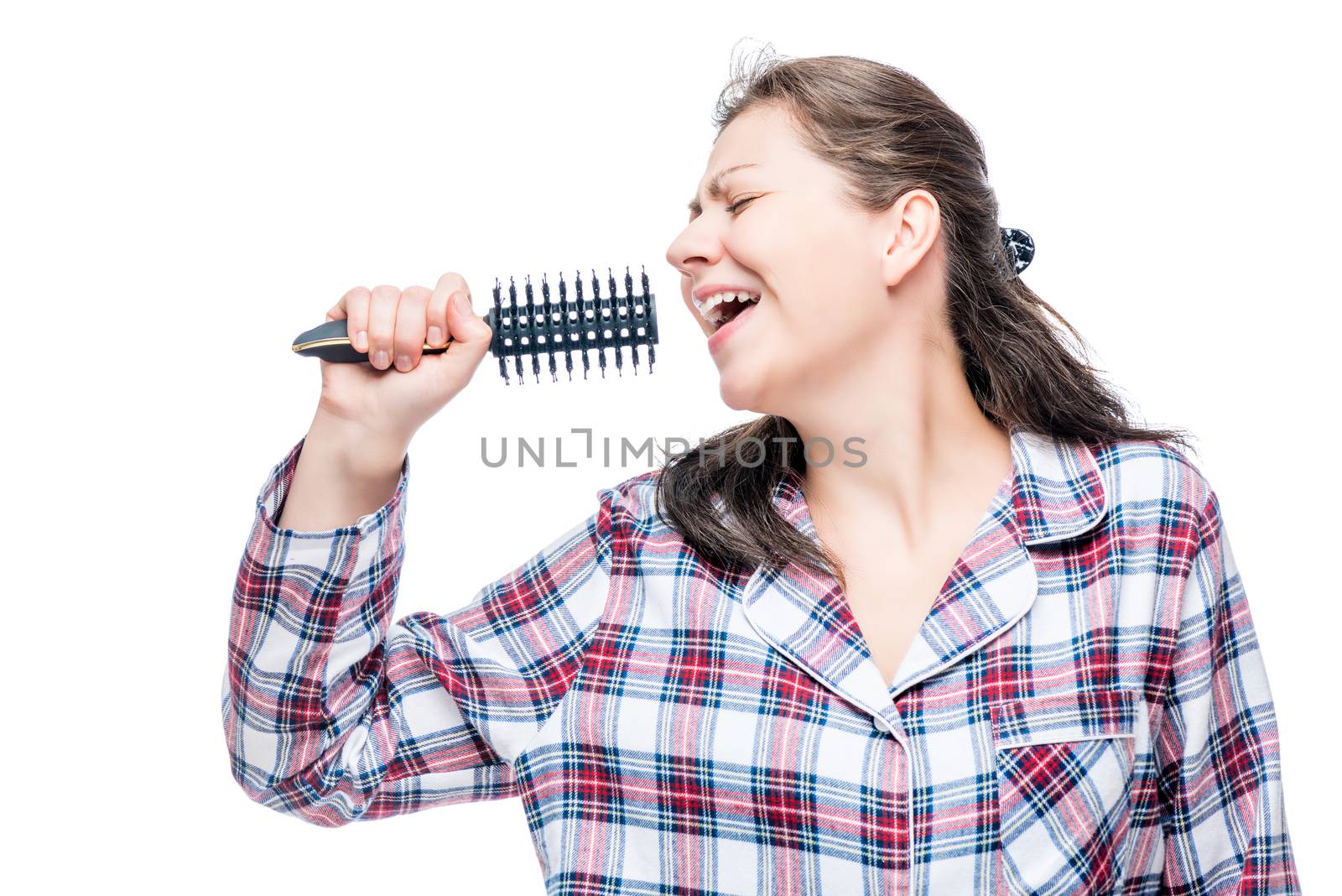 Woman in pajamas singing in hairbrush before going to bed on white background