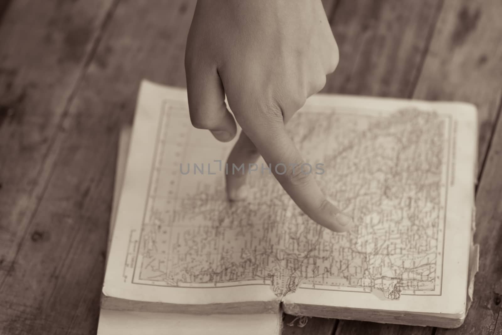 Fingers walking on the map in an old book. Selective focus image. Creative travel, hiking or geography learning concept. Toned sepia, vintage stylized photo