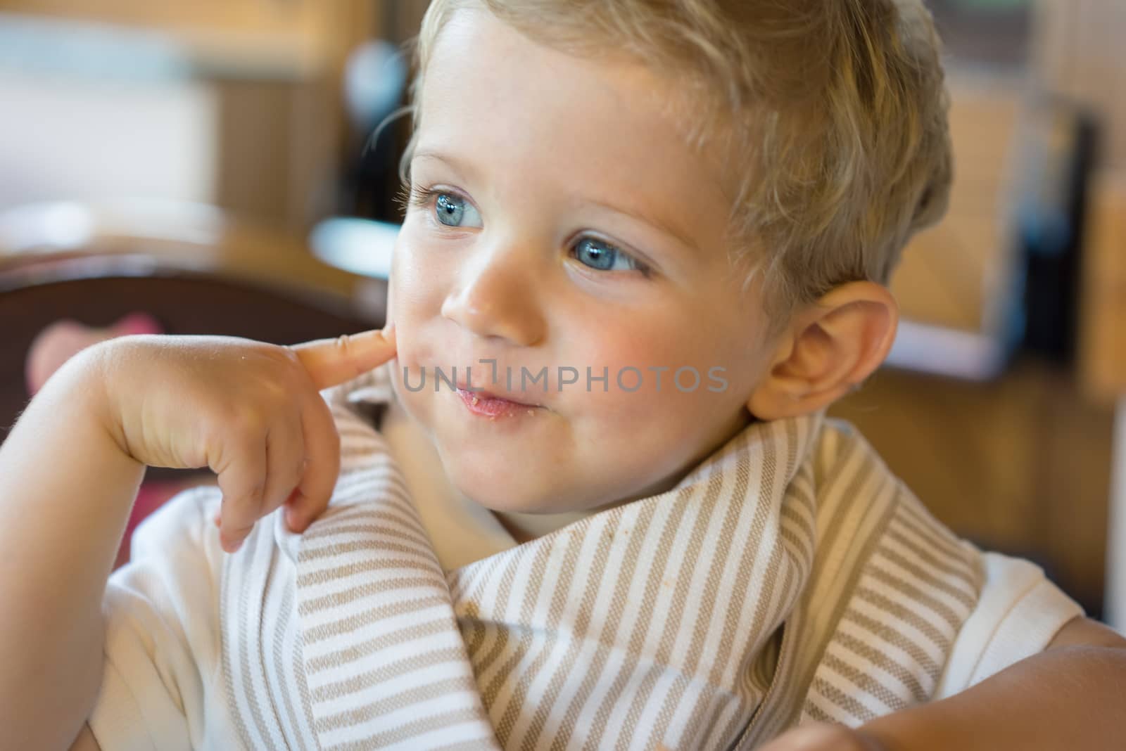 Happy baby boy (18 month) sitting in chair at restaurant, natural light.