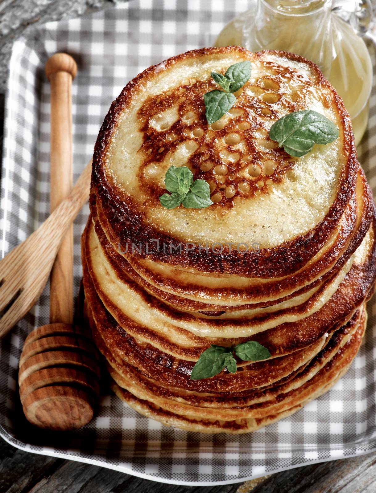 Stack of Homemade Pancakes with Mint Leafs, Honey, Wooden Fork and Honey Dipper closeup in Checkered Tray