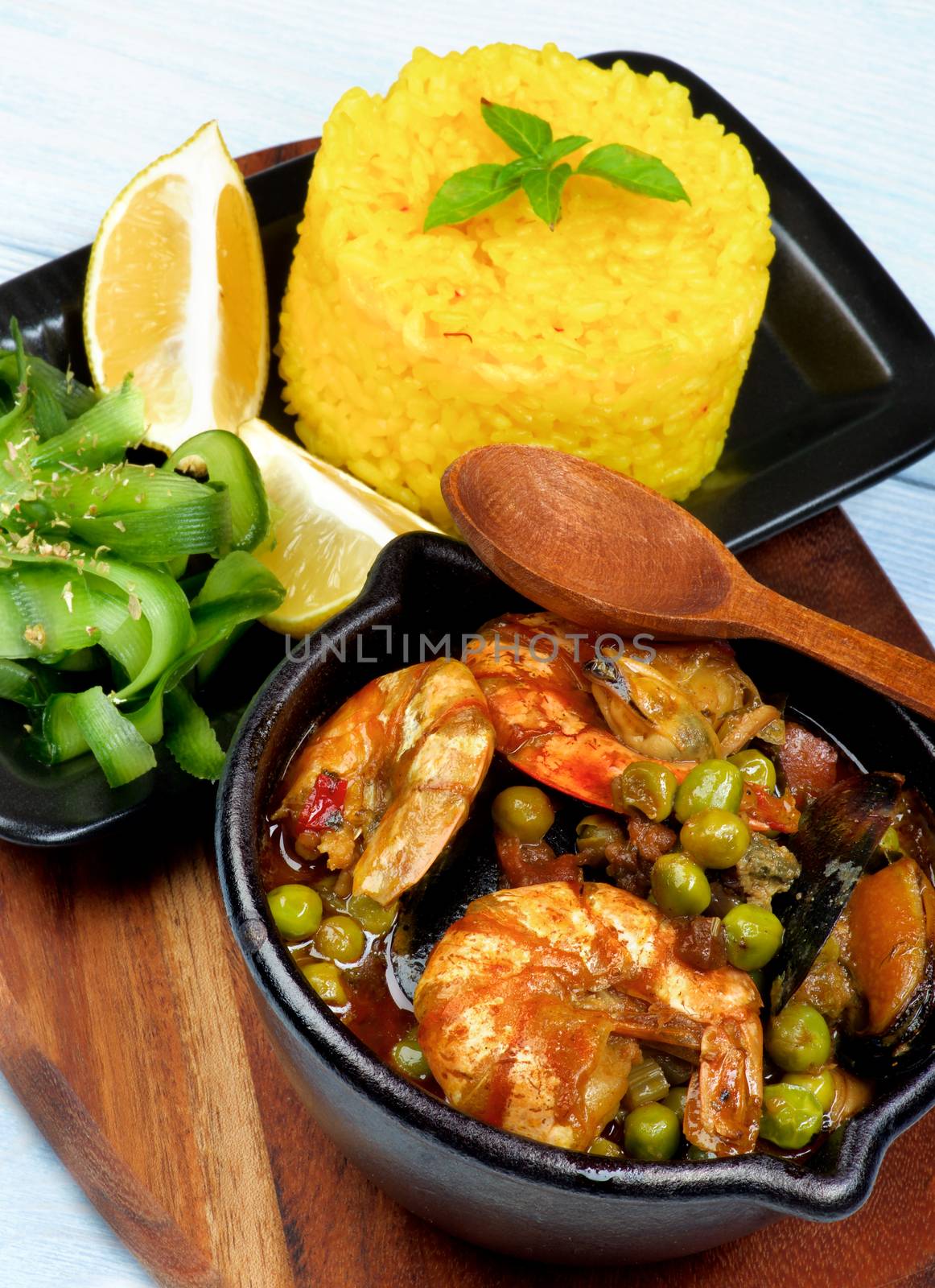 Delicious Seafood Curry with Saffron Rice, Cucumber Salad  and Lemon Served on Board closeup on Wooden background. Focus on Foreground