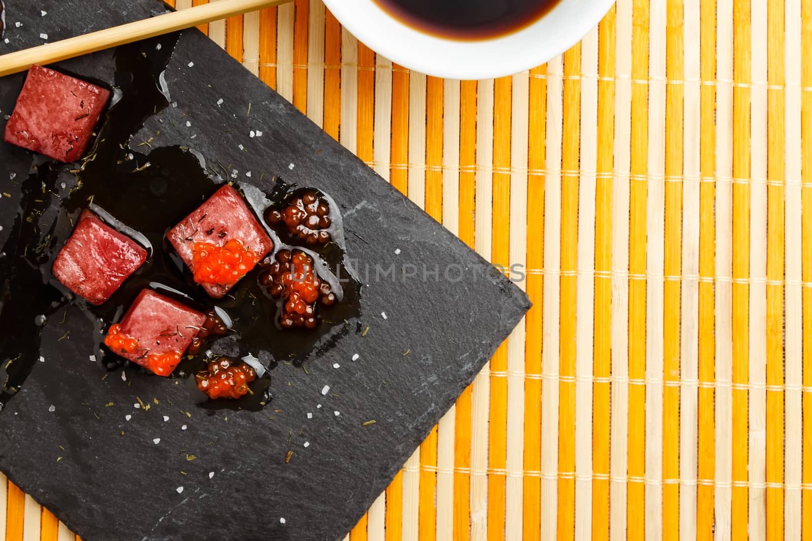 Tuna sashimi dipped in soy sauce with salmon roe, thick salt and dill on slate stone with chopsticks and bowl with soy viewed from above. Raw fish in traditional Japanese style. Horizontal image.