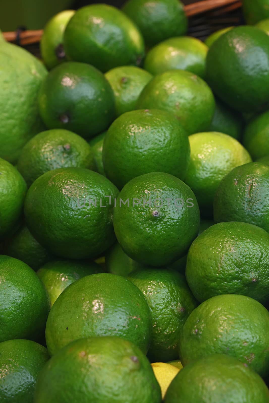 Heap of fresh green ripe lime fruits on retail market stall display, close up, high angle view