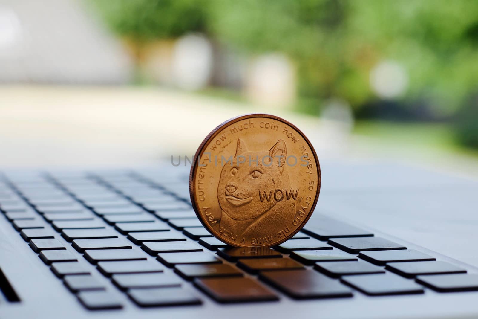 Digital currency physical brass dogecoin coin on the black computer keyboard near the window.