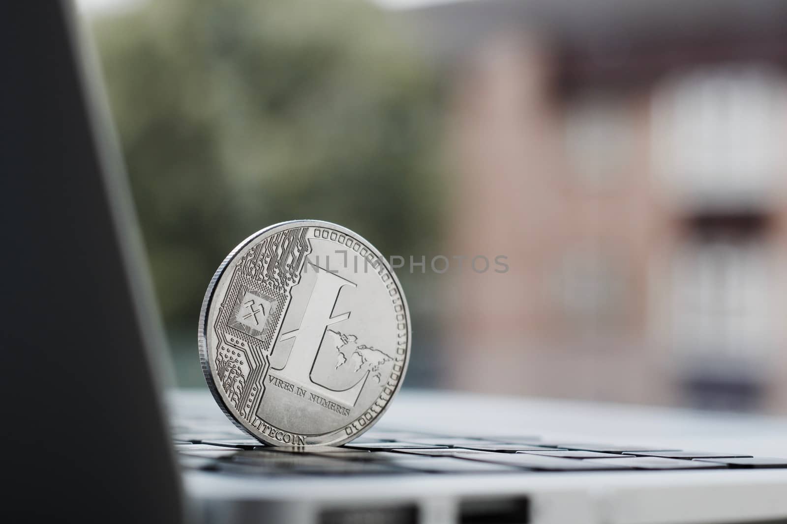 Cryptocurrency physical silver Litecoin coin on the black computer keyboard near the window.