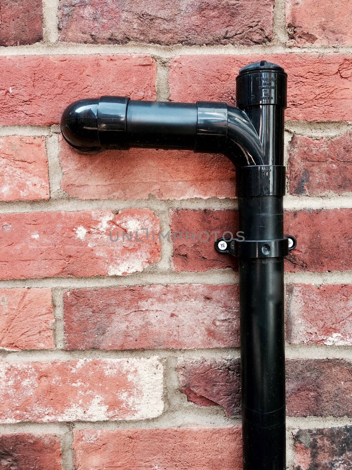 Black sewage pipe outdoor on old brick wall.