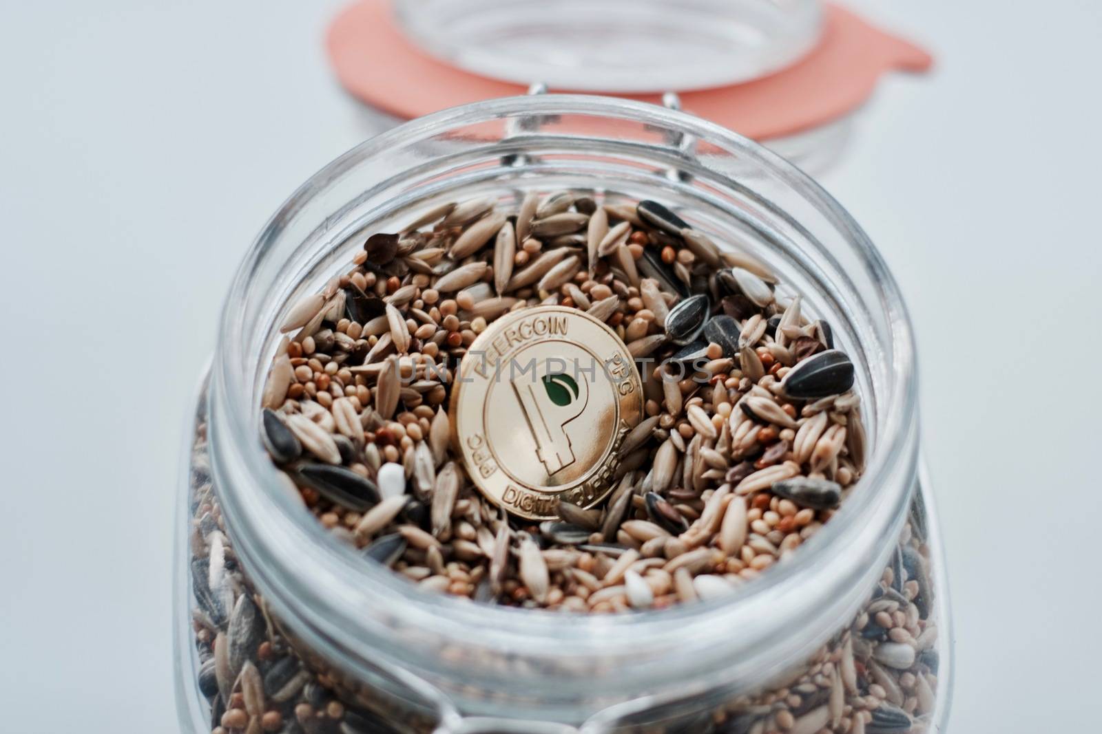 Cryptocurrency physical gold peercoin coin and seeds in glass jar.