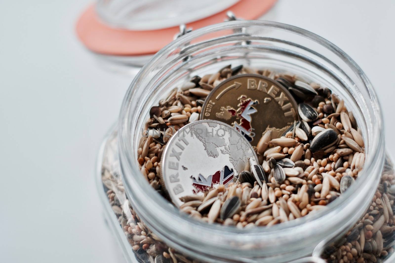 Two gold and silver brexit coins in glass jar with natural seeds.