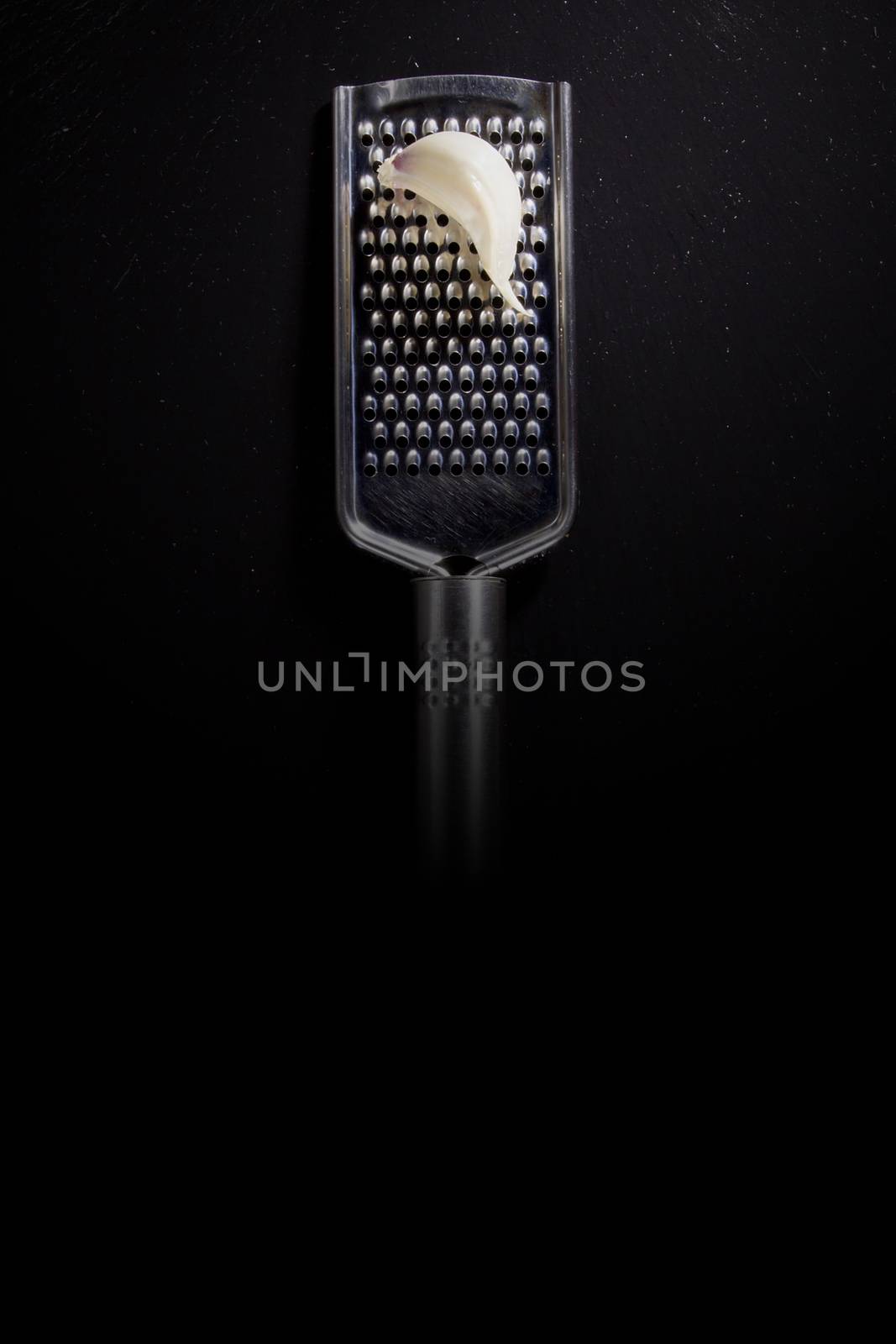 Metallic shiny grater and garlic on a black background