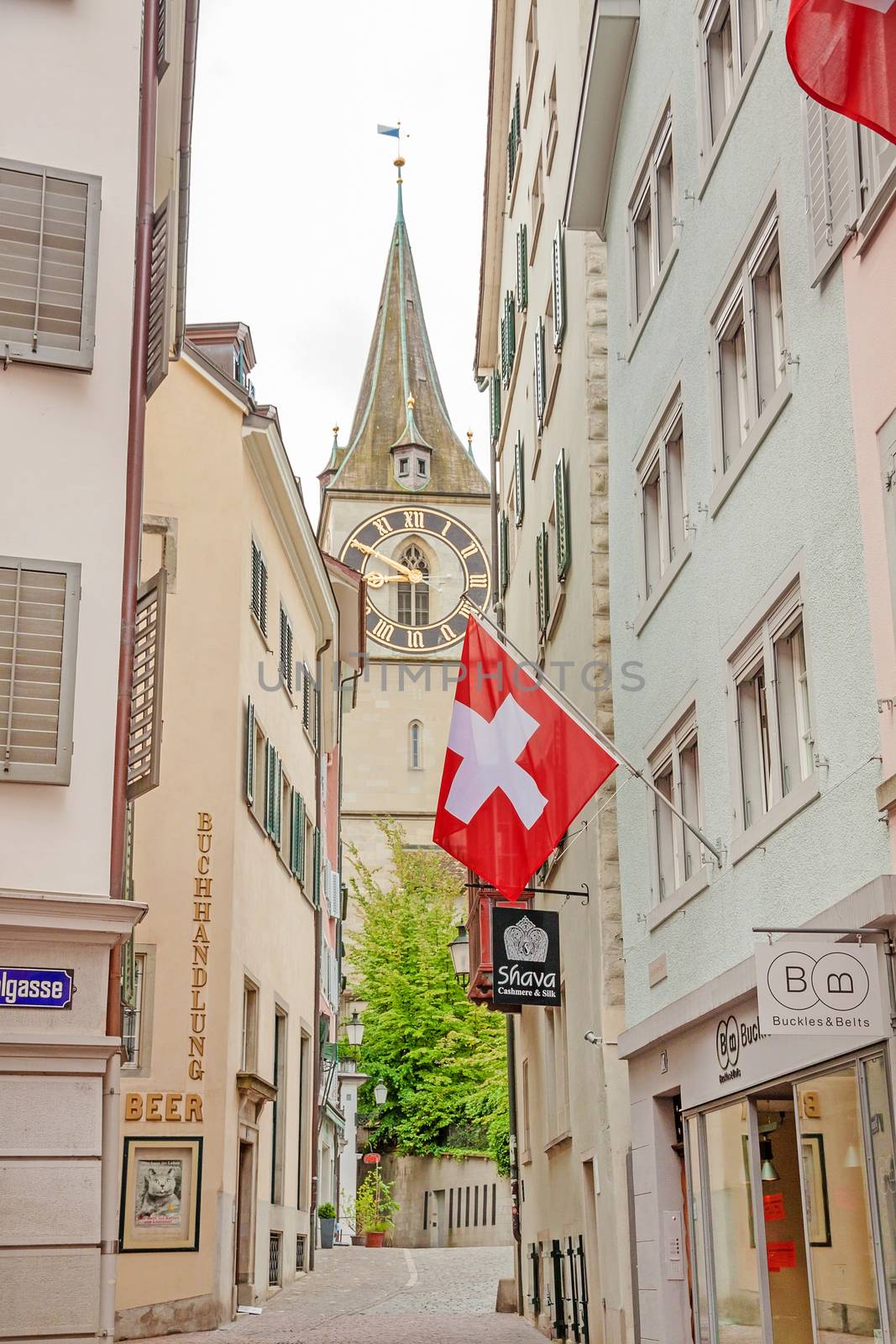 Zurich, Switzerland - June 10, 2017: St. Peter church, downtown Zurich, view from alley with swiss flag.