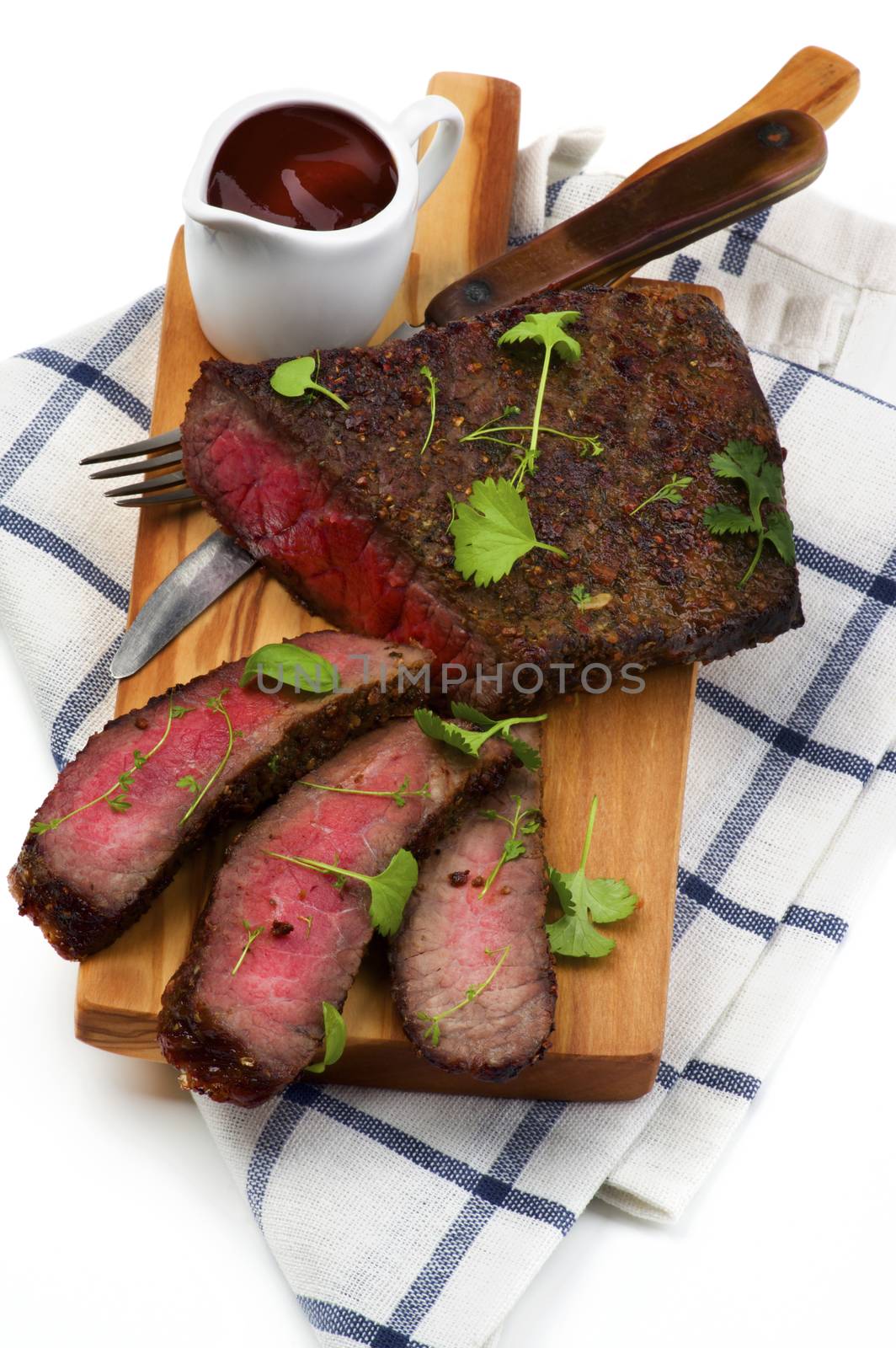 Delicious Roast Beef Medium Rare Sliced on Wooden Cutting Board with Tomato Sauce, Fork and Table Knife closeup on Checkered Napkin