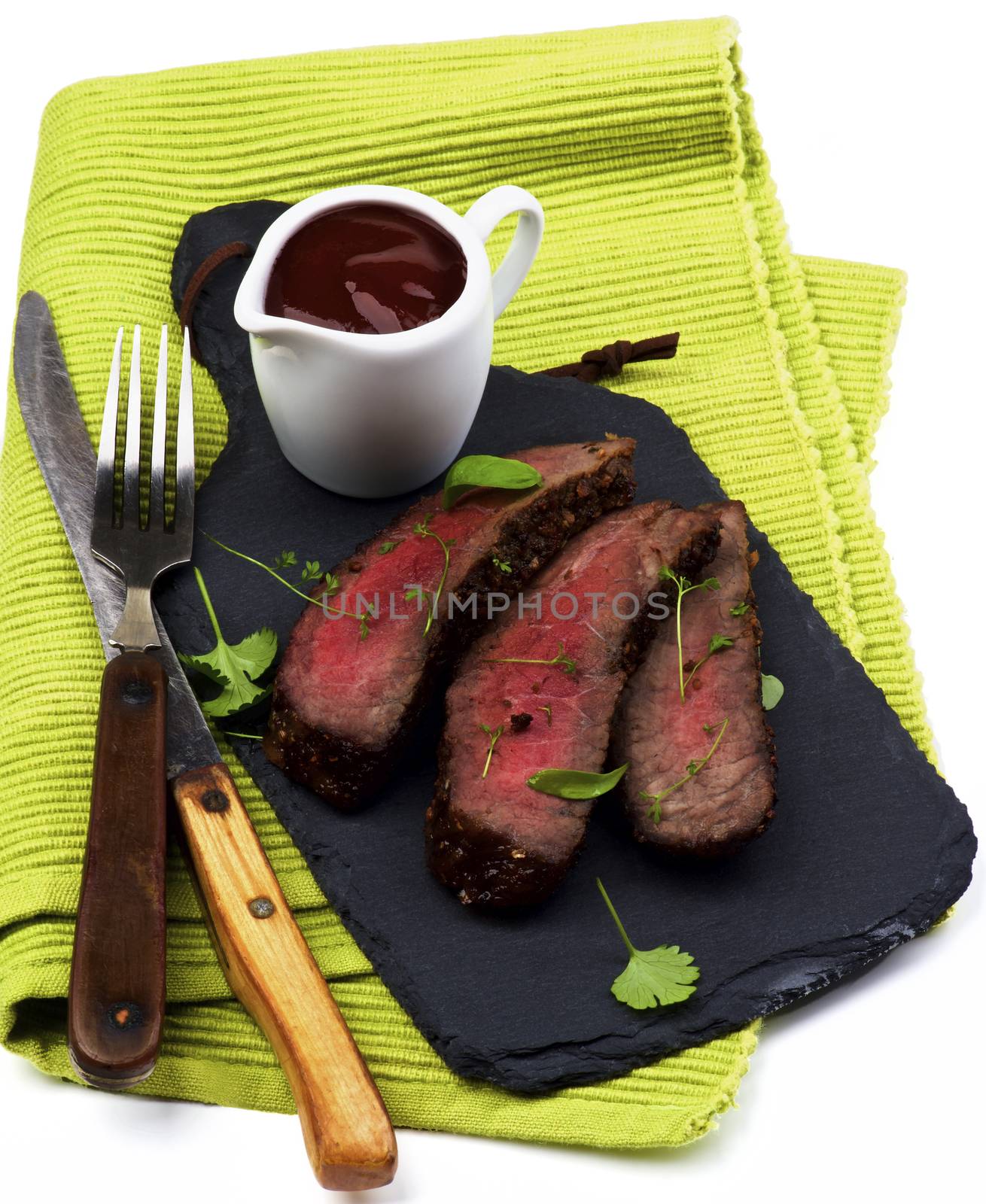 Slices of Delicious Roast Beef Medium Rare on Slate Serving Board with Tomato Sauce, Fork and Table Knife closeup on Green Napkin
