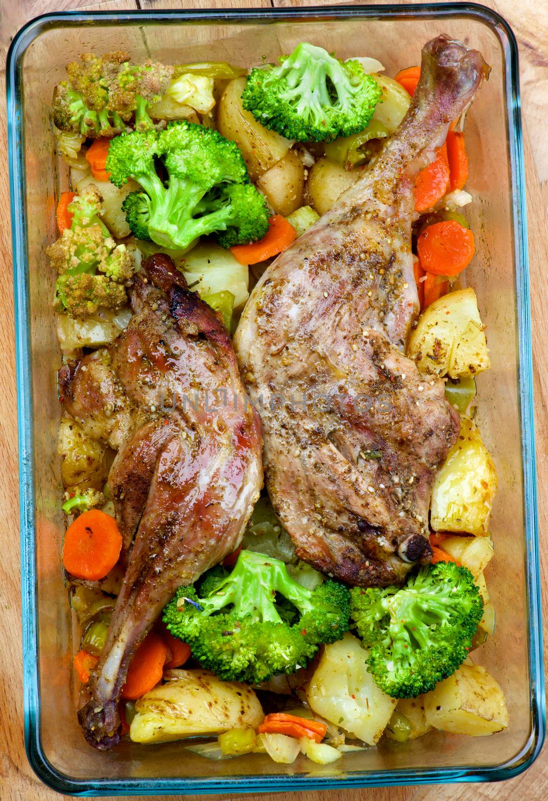 Delicious Oven-Baked Duck Legs with Potatoes, Carrot, Leek and Broccoli into Glass  Tray closeup on Wooden background