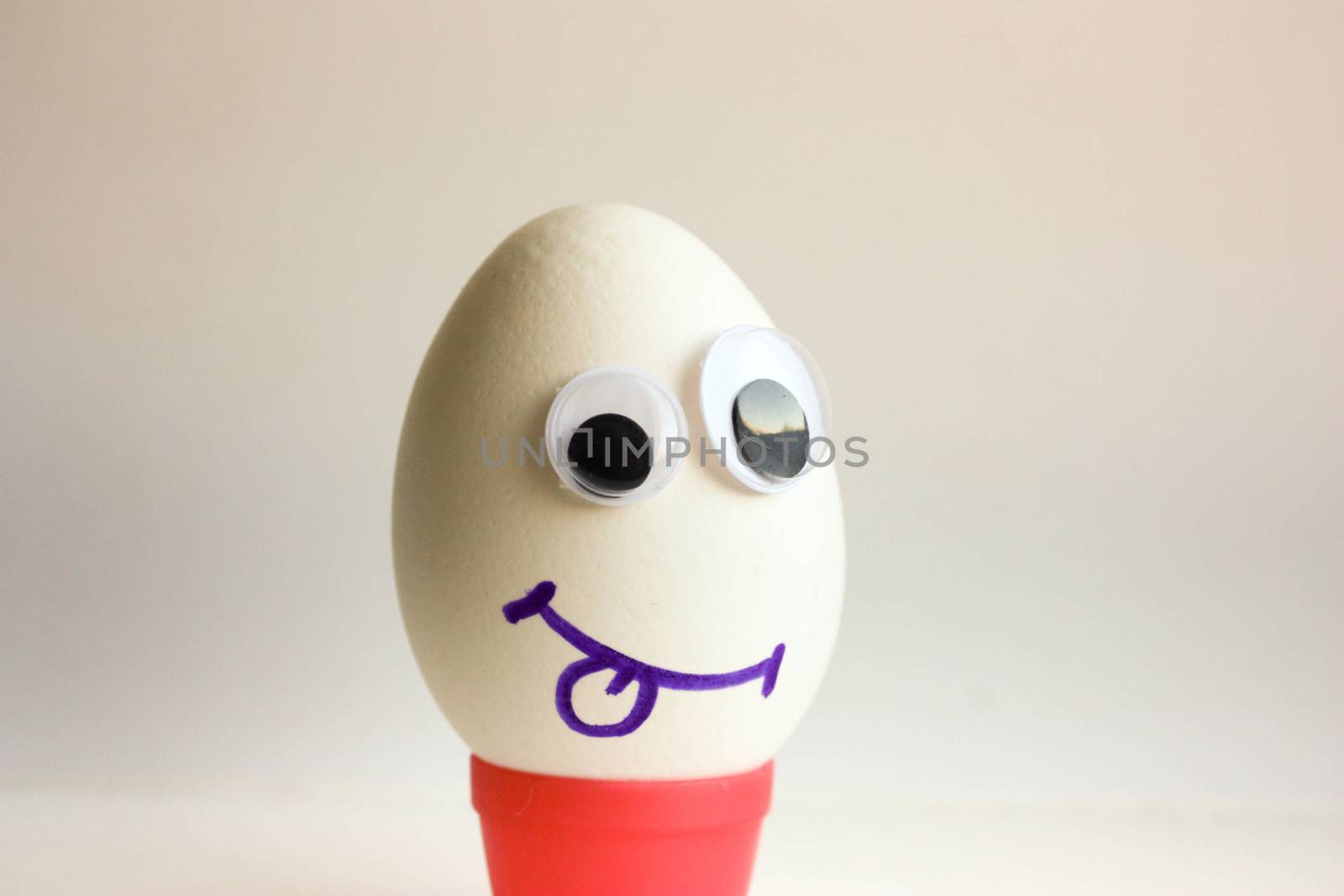 An egg to show the tongue. Egg with a funny painted face on a white background. Photo for your design.