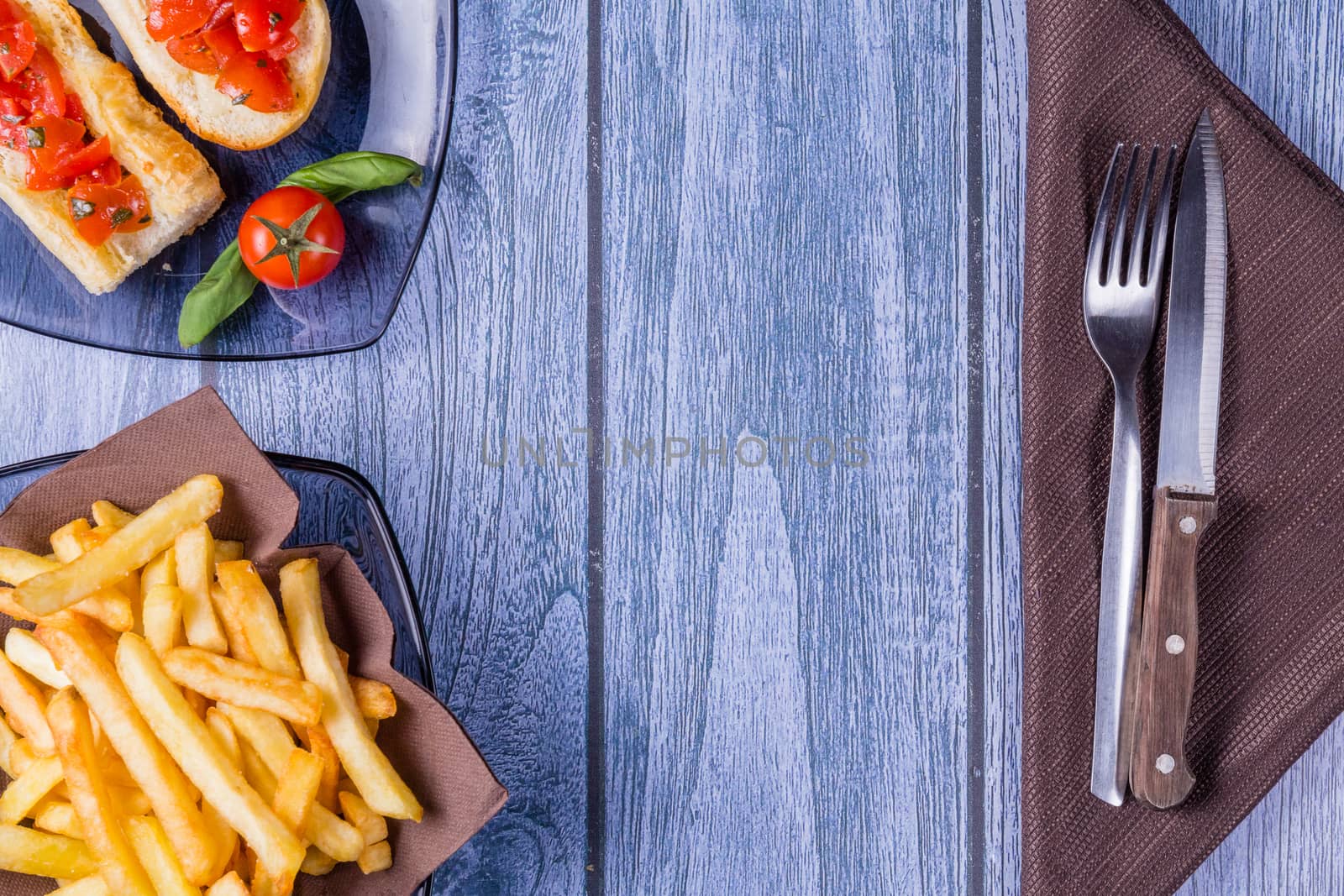 Italian bruschetta, a grilled crusty bread with tomatoes in pieces, basil and mozzarella cheese and a plate of french fries