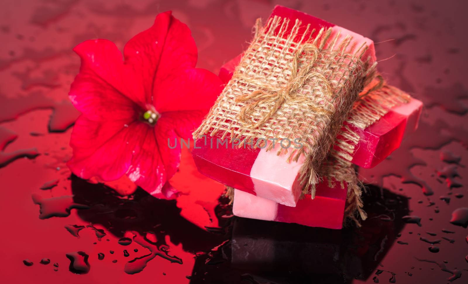 Handmade soap red with a flower petunia on red background and drops of water