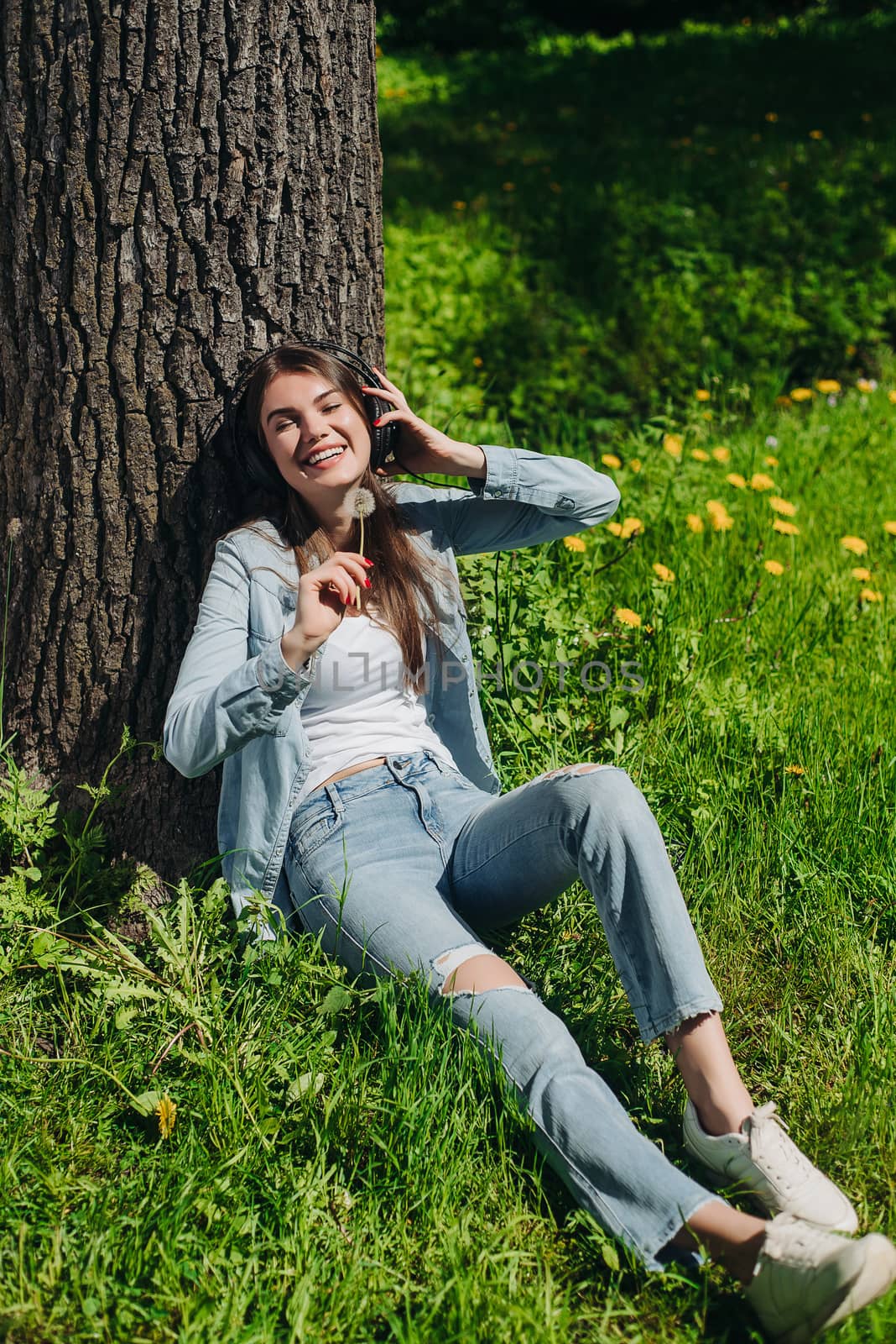 Young brunette woman with headphones listening to the music in park on sunny summer day