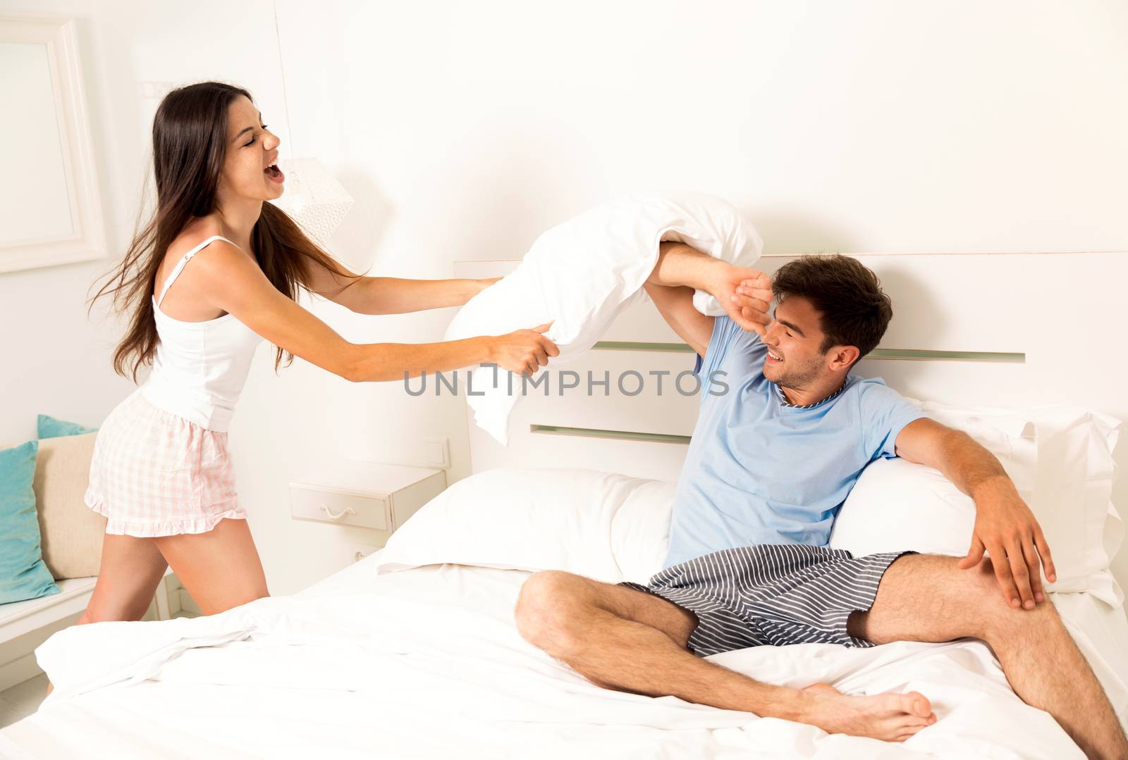 Young couple playing the bed and fighting with pillows