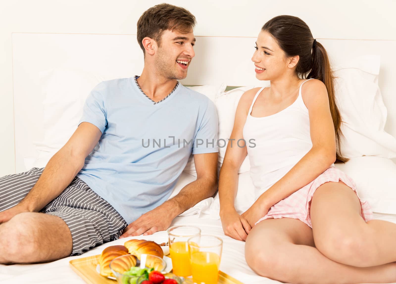 Young couple siting on the bed and ready to eat the breakfast