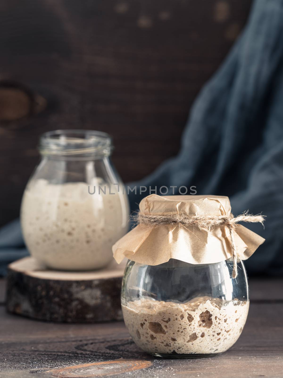 Active rye and wheat sourdough starter in glass jar on brown wooden background. Starter for sourdough bread. Toned image. Copy space. Vertical