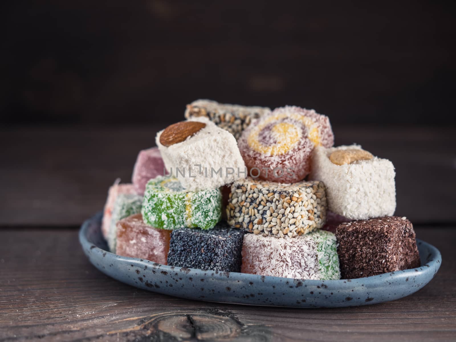 Closeup view of assortment turkish delight in blue trandy plate on dark wooden background. Copy space. Low key
