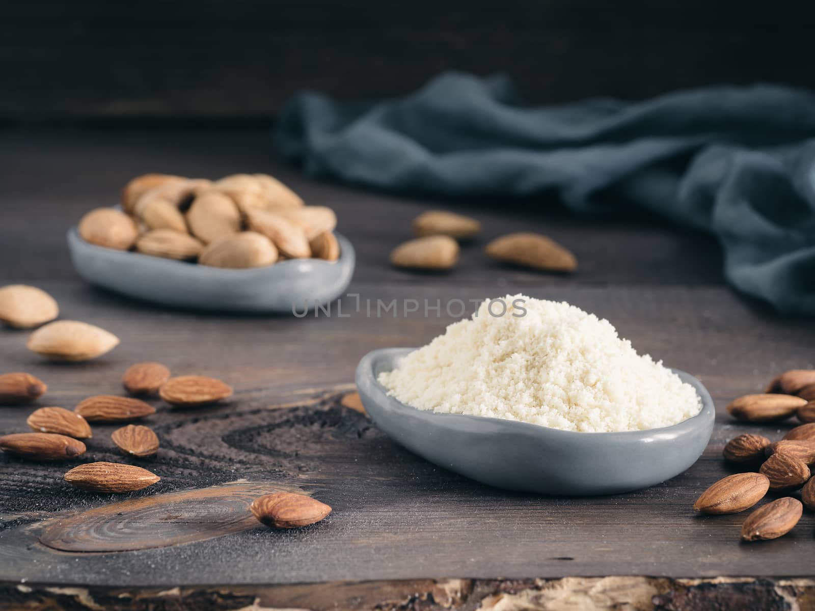 Almond powder in gray trendy plate and almonds on dark wooden table. Almond flour and peeled kernel almonds. Copy space.