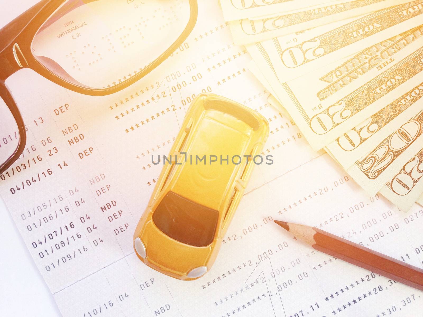 Business, finance, savings, banking or car loan concept : Miniature car model, pencil, eyeglasses, money and savings account passbook or financial statement on white background