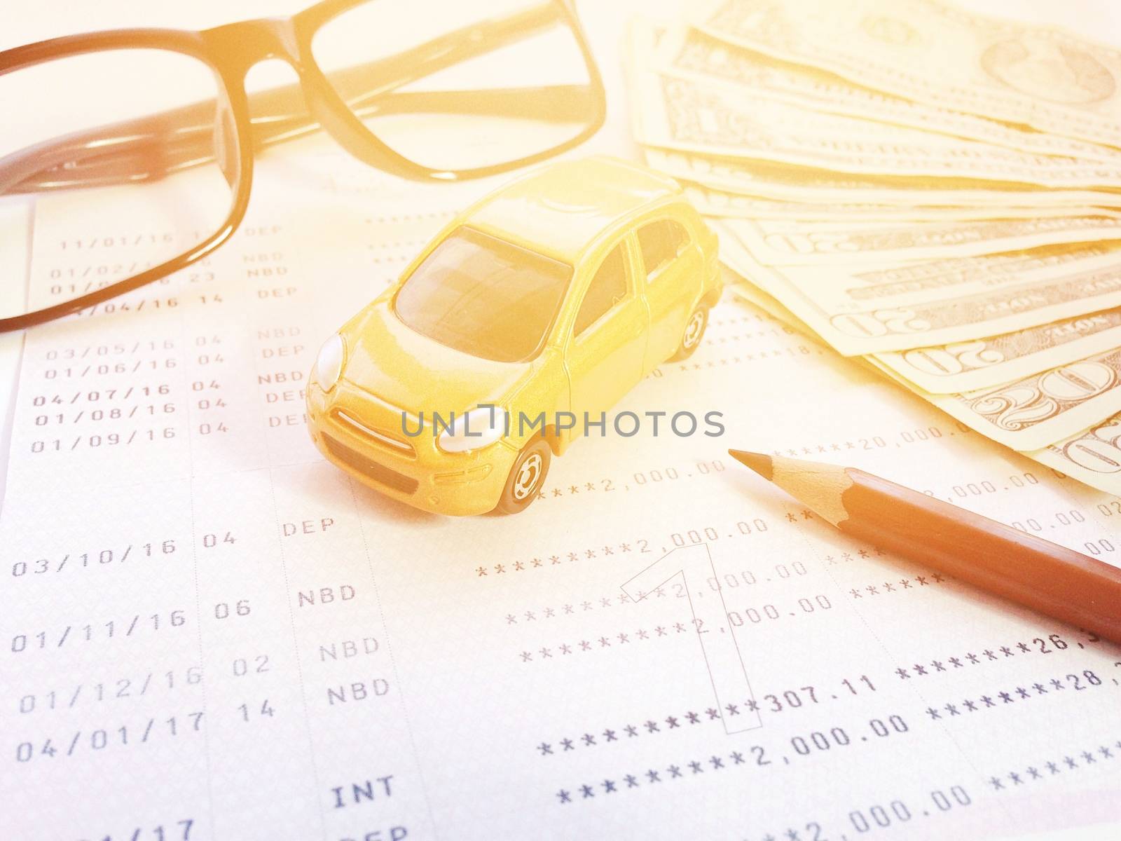 Business, finance, savings, banking or car loan concept : Miniature car model, pencil, eyeglasses, money and savings account passbook or financial statement on white background