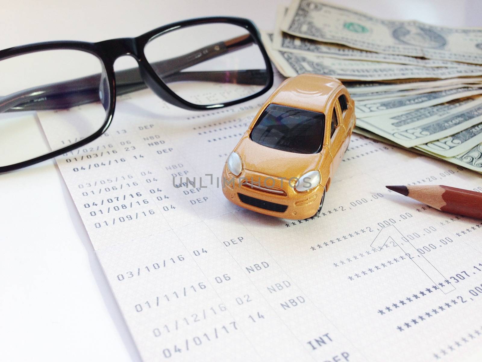 Business, finance, savings, banking or car loan concept : Miniature car model, pencil, eyeglasses, money and savings account passbook or financial statement on white background