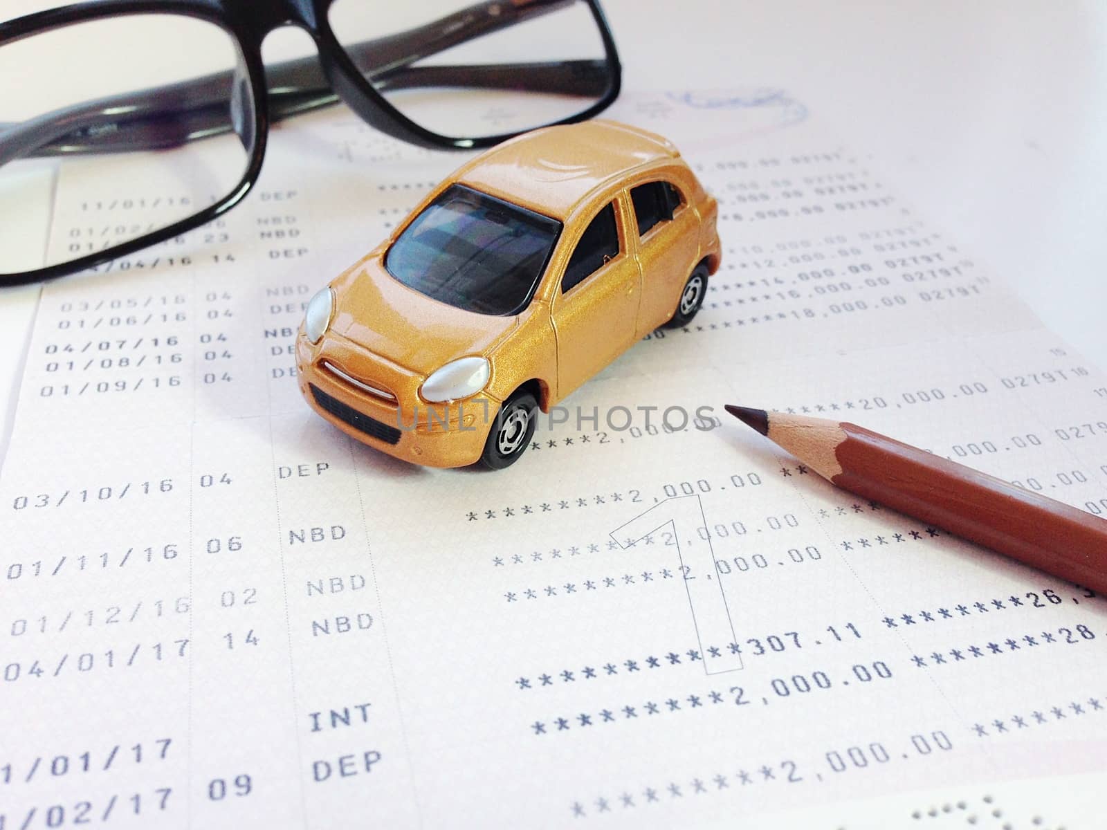 Business, finance, savings, banking or car loan concept : Miniature car model, pencil, eyeglasses and savings account passbook or financial statement on white background